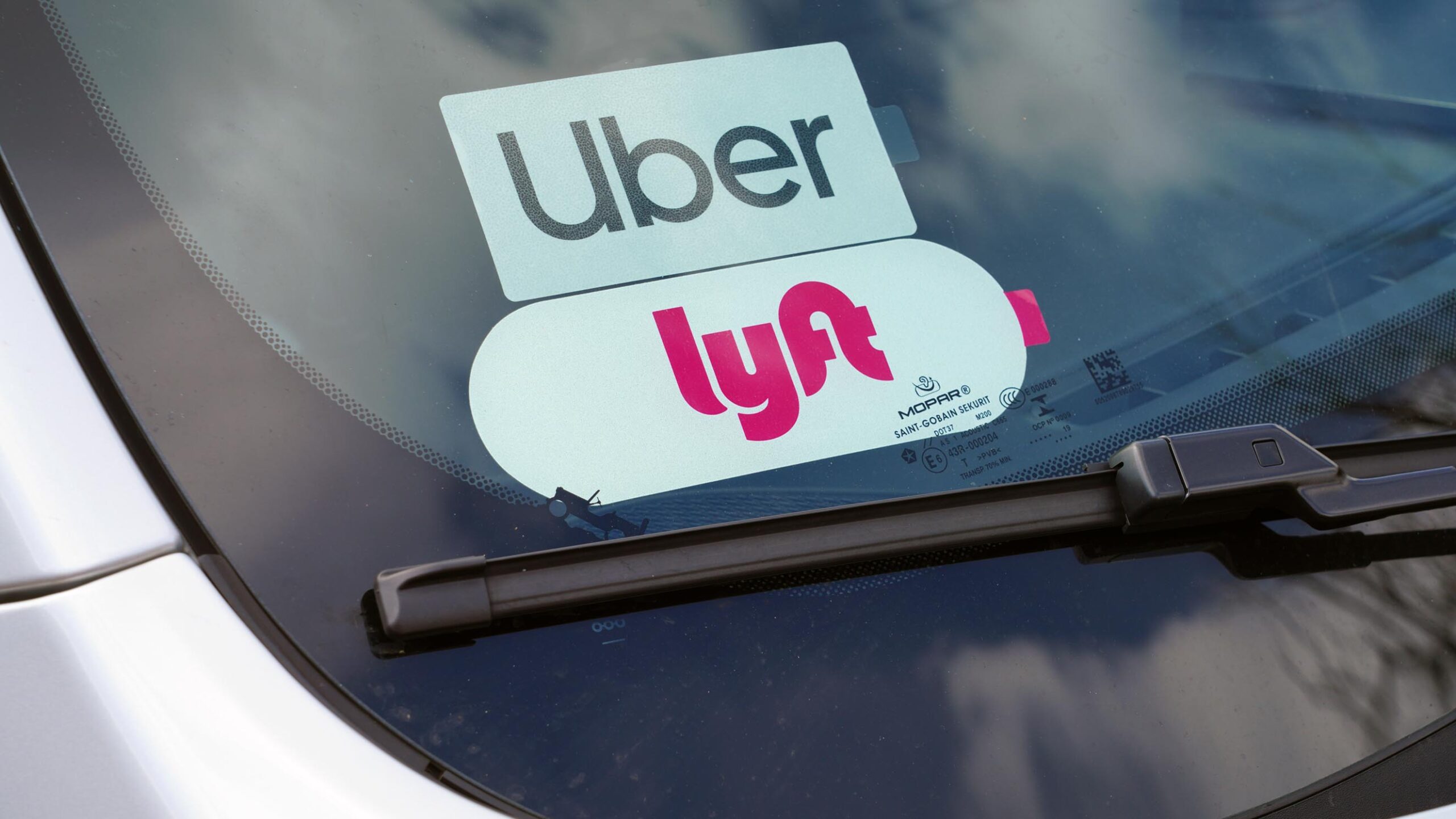 Lyft and Uber ridesharing stickers in the window of a white sedan