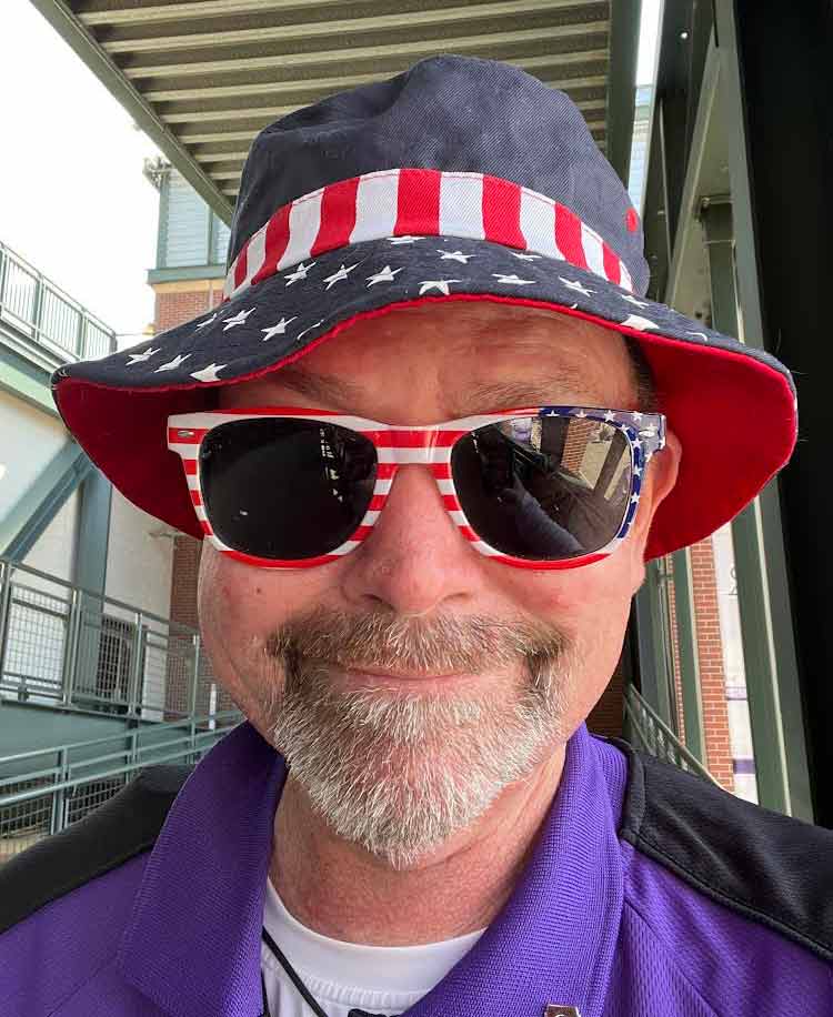 A photo of our Coors Field Contributor Kyle in a bucket hat and sunglasses, both sporting American flag patterns