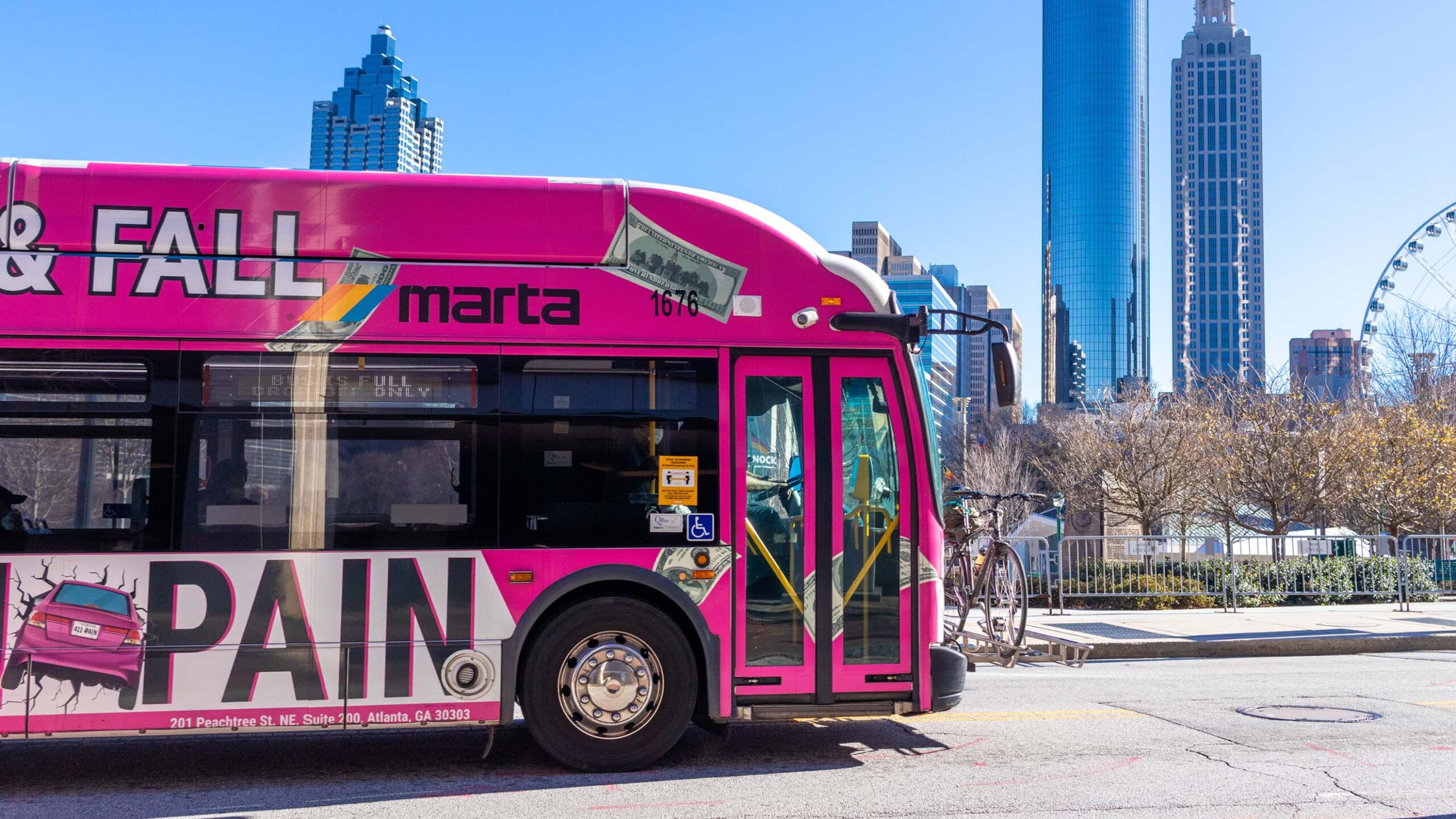 A bright pink MARTA bus in Atlanta drives down the road with Olympic Centennial Park in the background