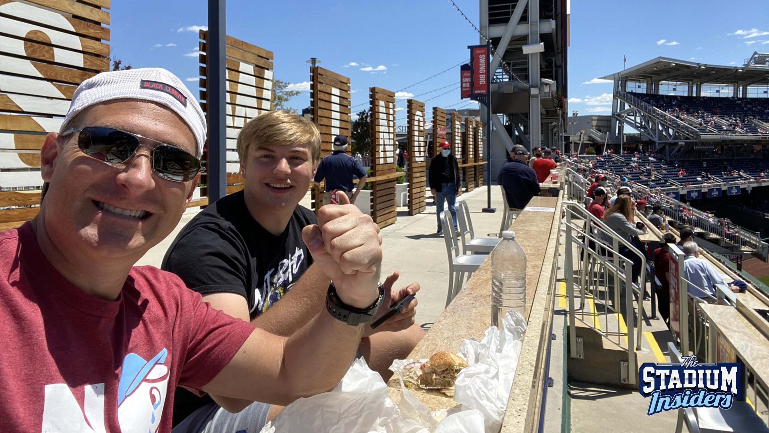 Two smiling men sit at a railing at Nationals Park